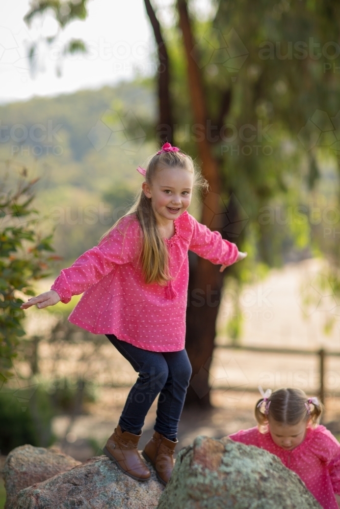 Young girl with long pony tail playing on rocks outdoors - Australian Stock Image