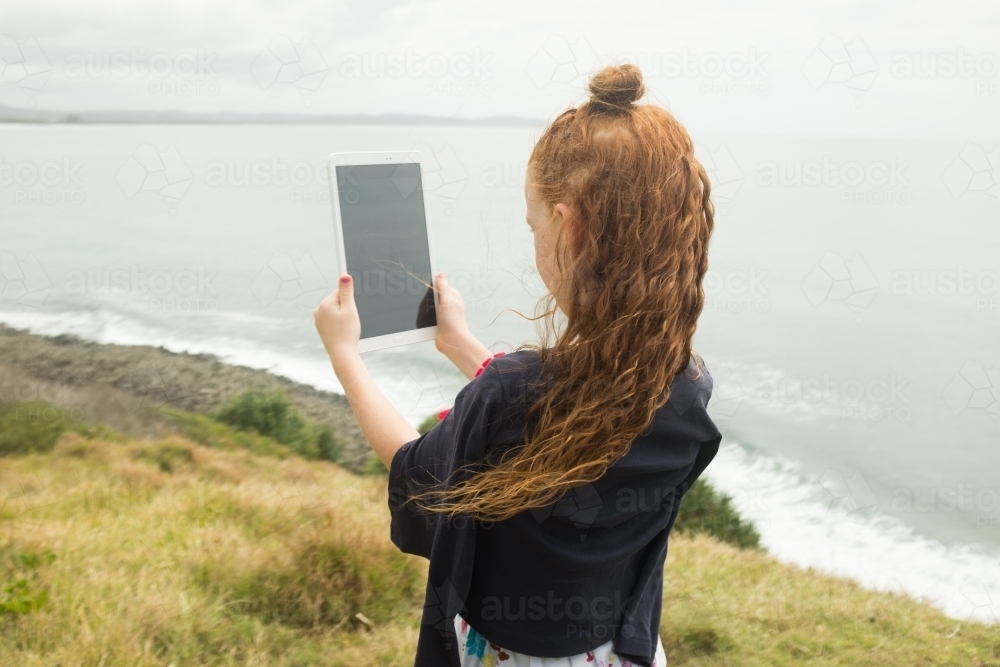Young girl with long red hair using a tablet at a lookout - Australian Stock Image