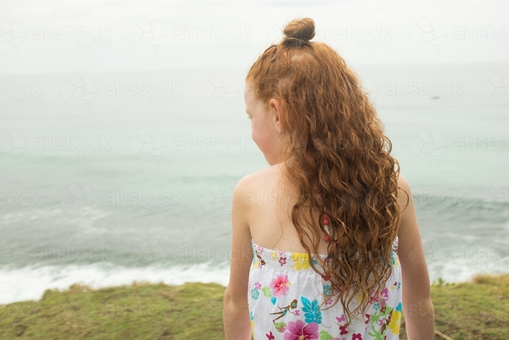 Young girl with long red hair watching the ocean - Australian Stock Image