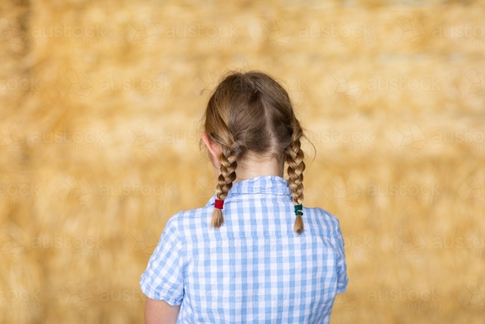 young girl with plaits seen from behind wearing blue checked blouse - Australian Stock Image