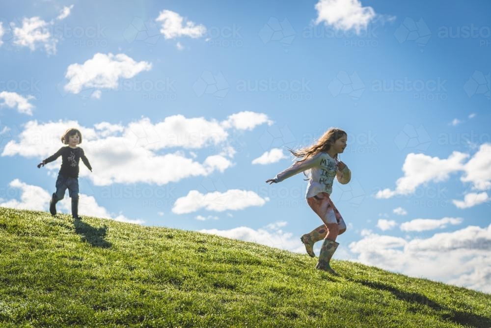 Young girls running down a grassy hill - Australian Stock Image