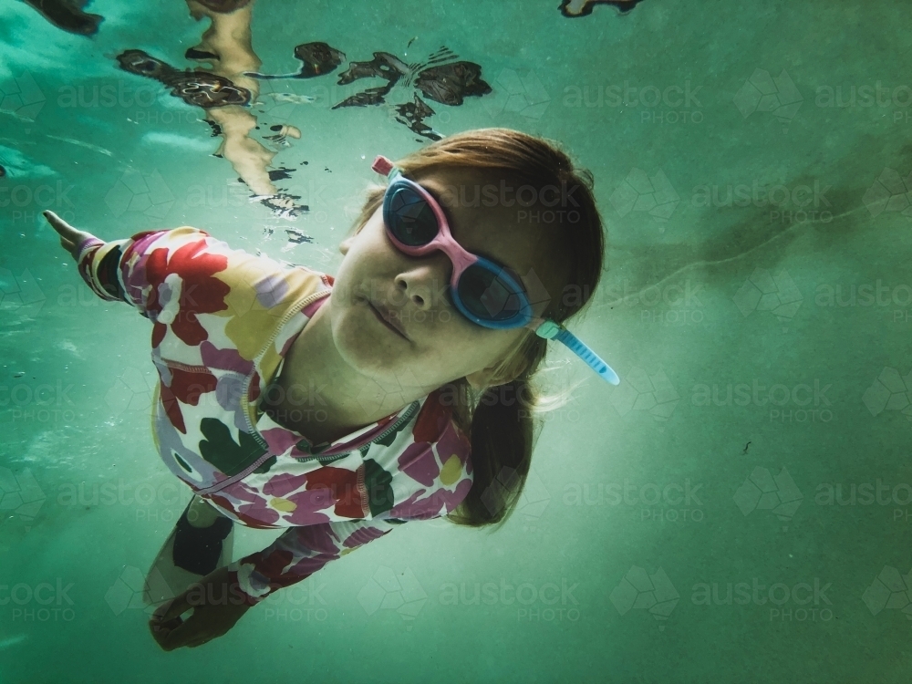 Young girls swimming underwater in pool wearing floral swim suit, goggles and fins - Australian Stock Image
