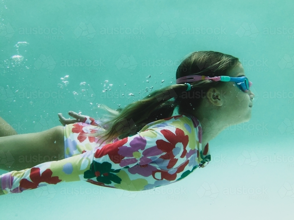 Young girls swimming underwater in pool wearing floral swimsuit and goggles - Australian Stock Image