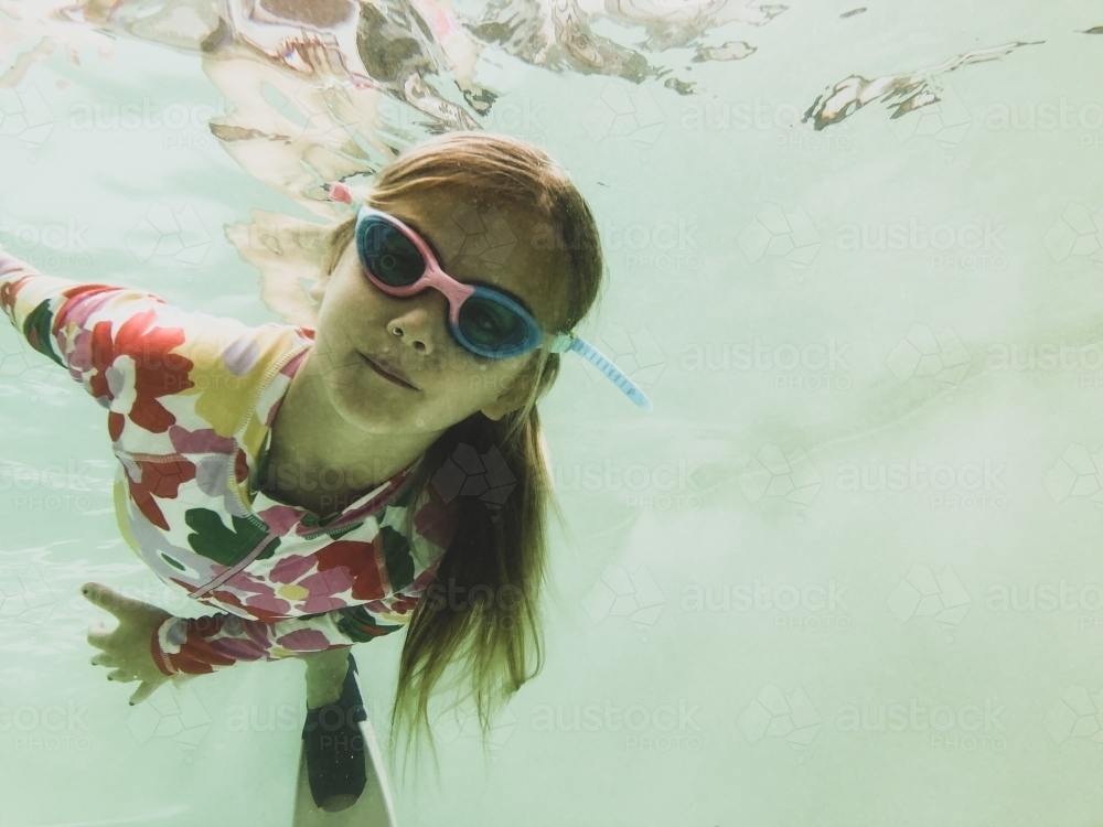 Young girls swimming underwater in pool wearing floral swimsuit, goggles and fins - Australian Stock Image