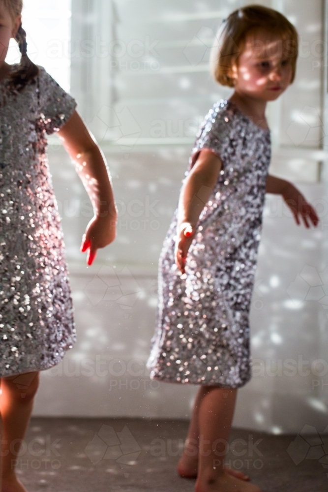 Young girls wearing sparkly dresses playing with the reflected light - Australian Stock Image