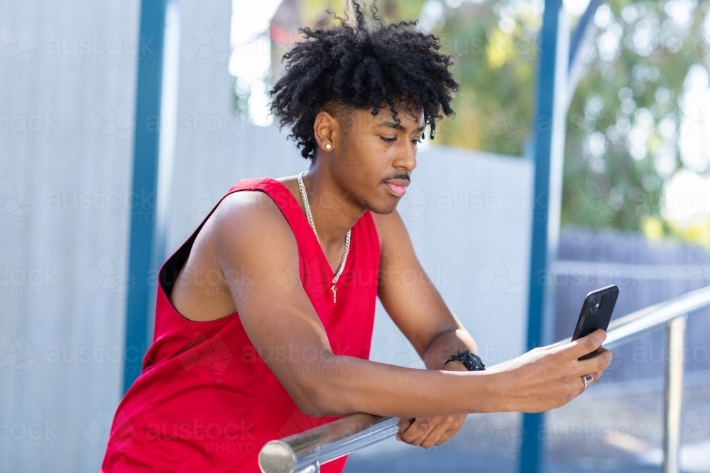 young guy looking at smartphone wearing red athletic singlet - Australian Stock Image