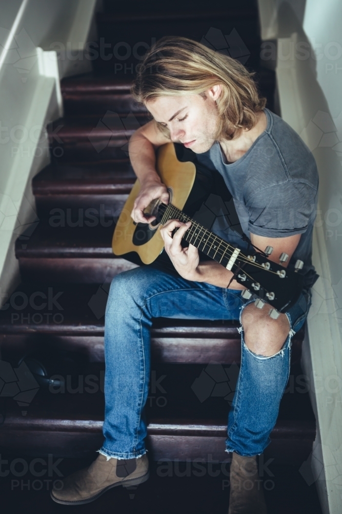Young guy playing guitar alone with a serious facial expression - Australian Stock Image
