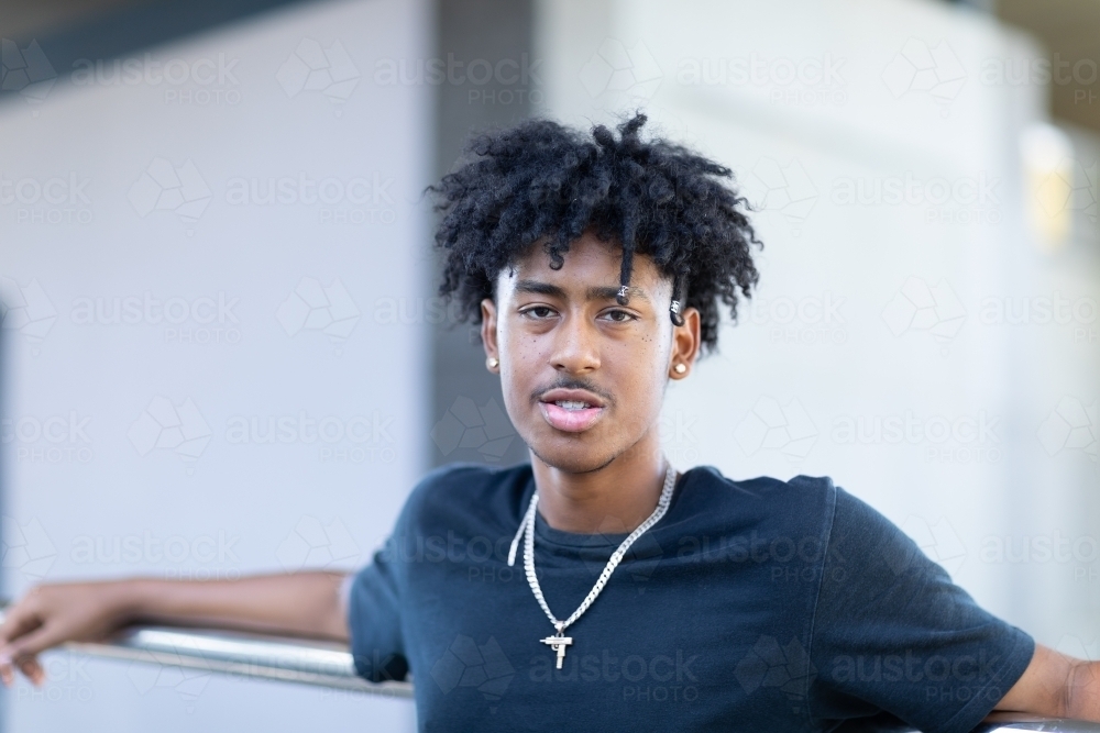 young guy with black tee-shirt and jewellery leaning on railing - Australian Stock Image