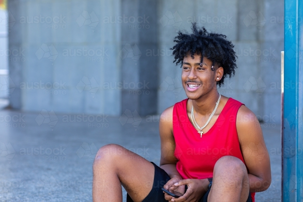 young guy with smartphone wearing red athletic singlet - Australian Stock Image
