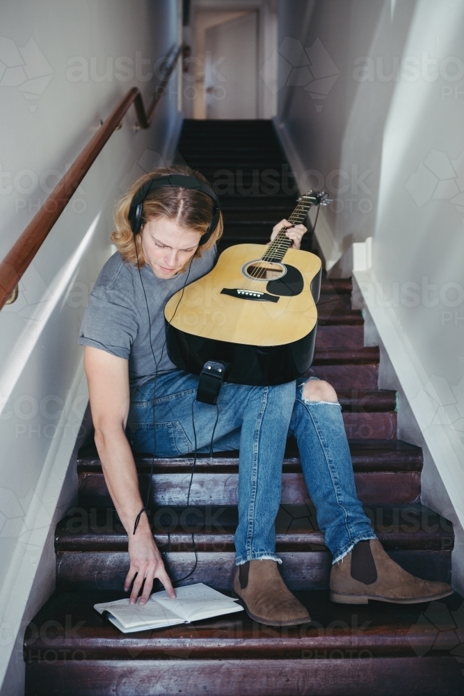 Young guy writing music on a staircase - Australian Stock Image