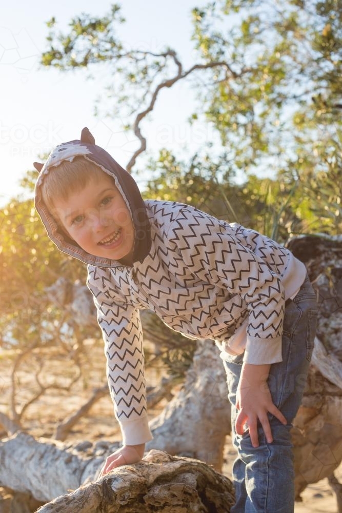 Young happy boy climbing fallen tree outdoors wearing hoodie - Australian Stock Image