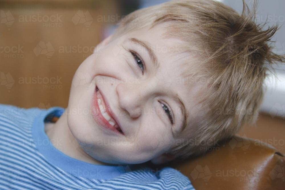 Young happy boy leaning on a leather couch smiling - Australian Stock Image
