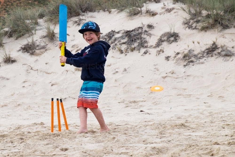 Young happy boy playing beach cricket - Australian Stock Image