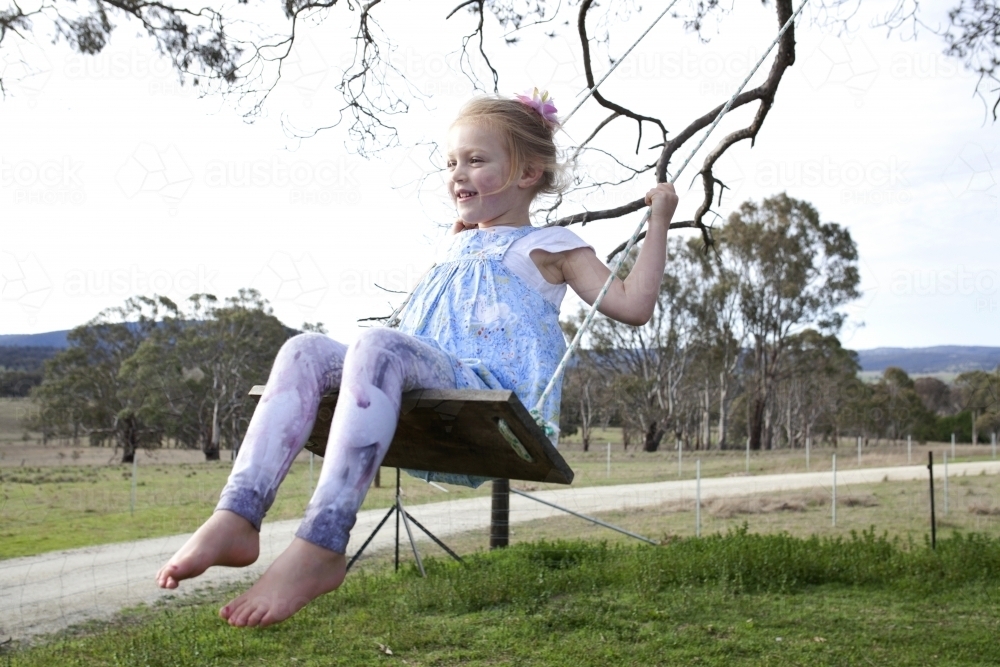 Young happy girl on tree swing in country backyard - Australian Stock Image