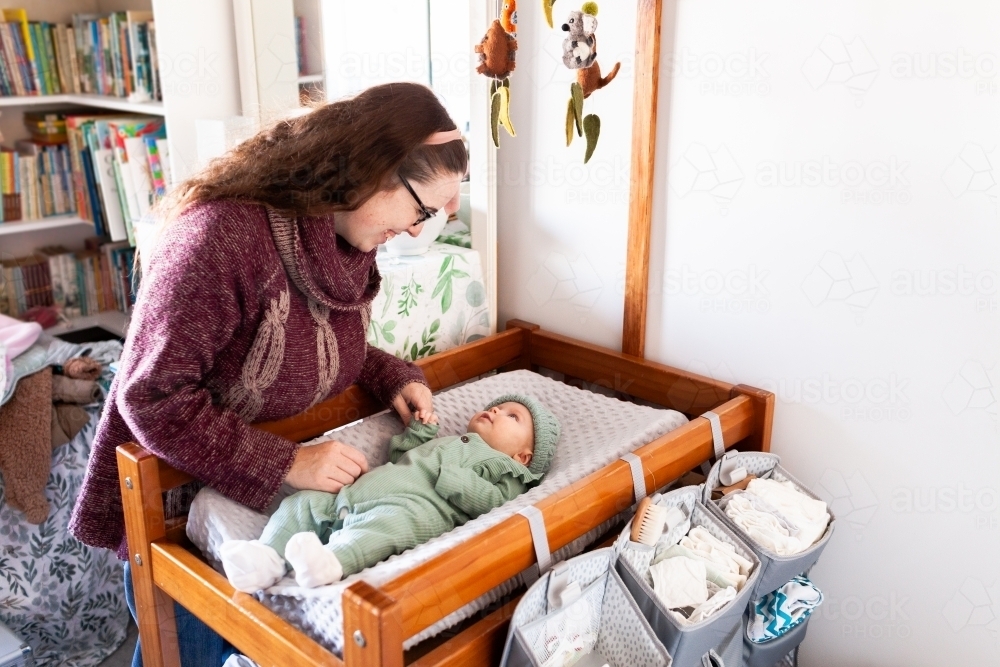 Young happy mum getting baby dressed for winter on change table in nursery - Australian Stock Image