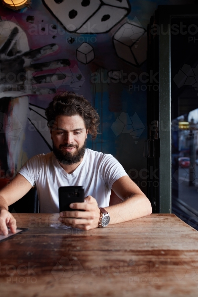 Young hipster man checking mobile phone at bar - Australian Stock Image
