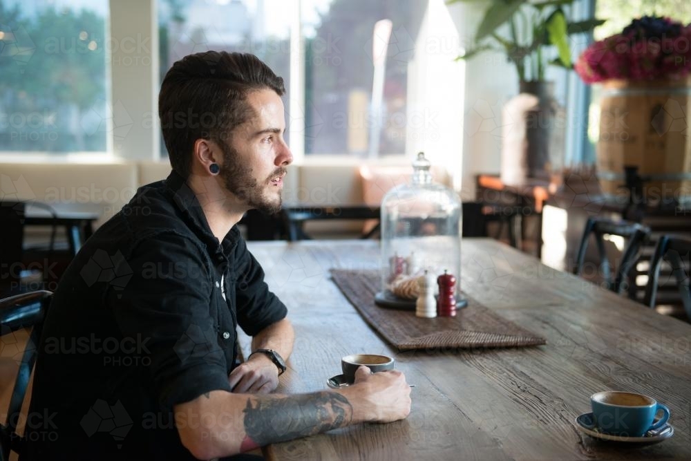 Young hipster man drinking coffee in a modern cafe - Australian Stock Image