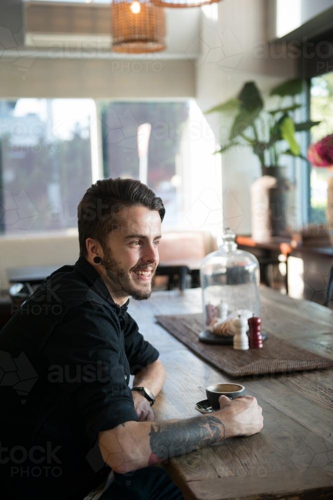 Young hipster man drinking coffee in a modern cafe - Australian Stock Image