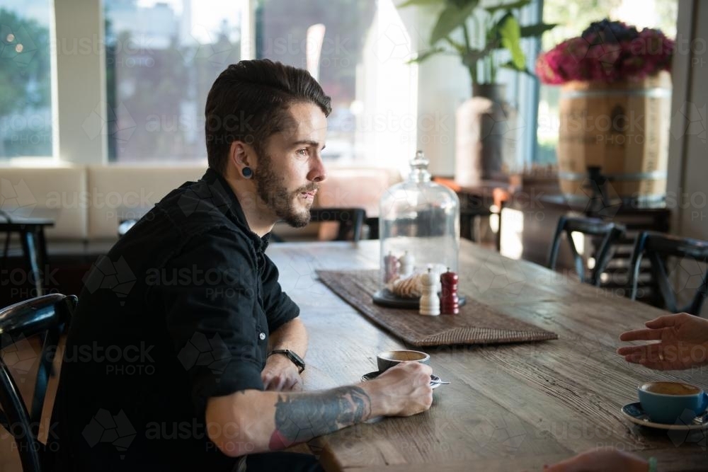 Young hipster sitting at table with coffee in a modern cafe - Australian Stock Image