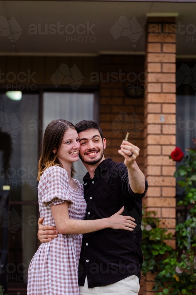 Young homeowners holding key first home hugging and smiling together - Australian Stock Image