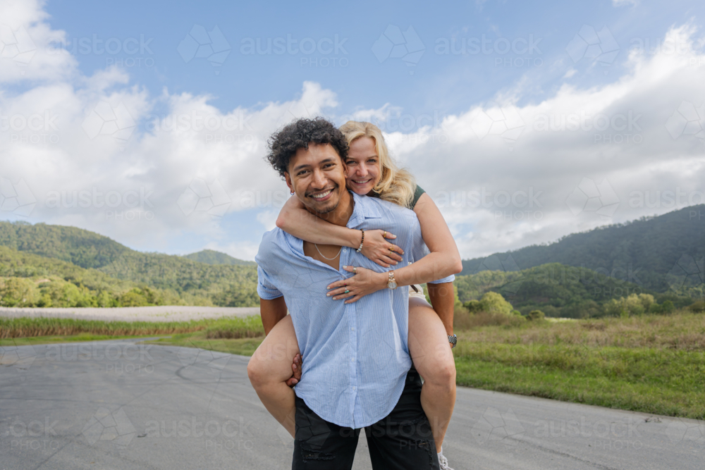 Young in love mixed race couple smiling during a piggyback ride - Australian Stock Image