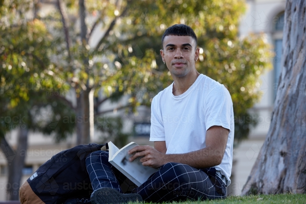 Young Indigenous Australian man enjoying  reading time outdoors - Australian Stock Image