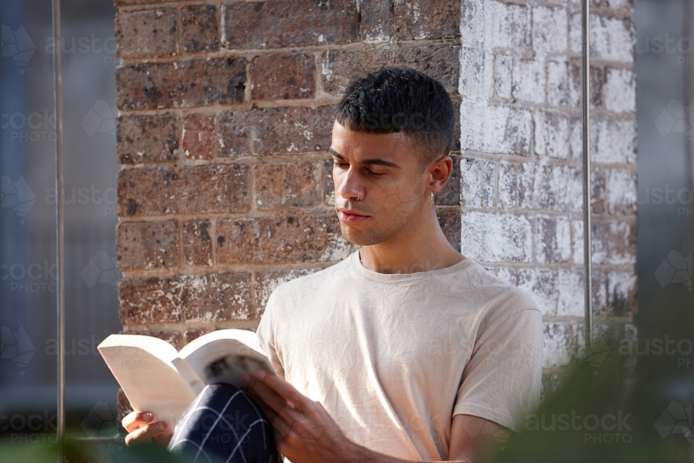 Young Indigenous Australian man enjoying reading time outdoors - Australian Stock Image