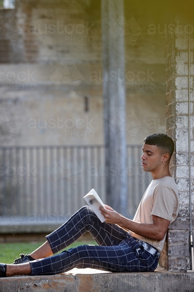 Young Indigenous Australian man enjoying  reading time outdoors - Australian Stock Image
