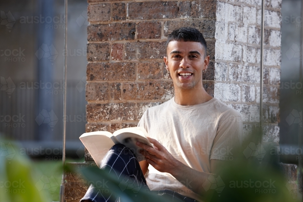Young Indigenous Australian man enjoying time outdoors with his book - Australian Stock Image
