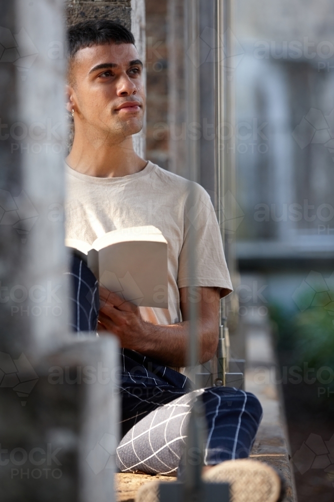 Young Indigenous Australian man enjoying time outdoors with his book - Australian Stock Image