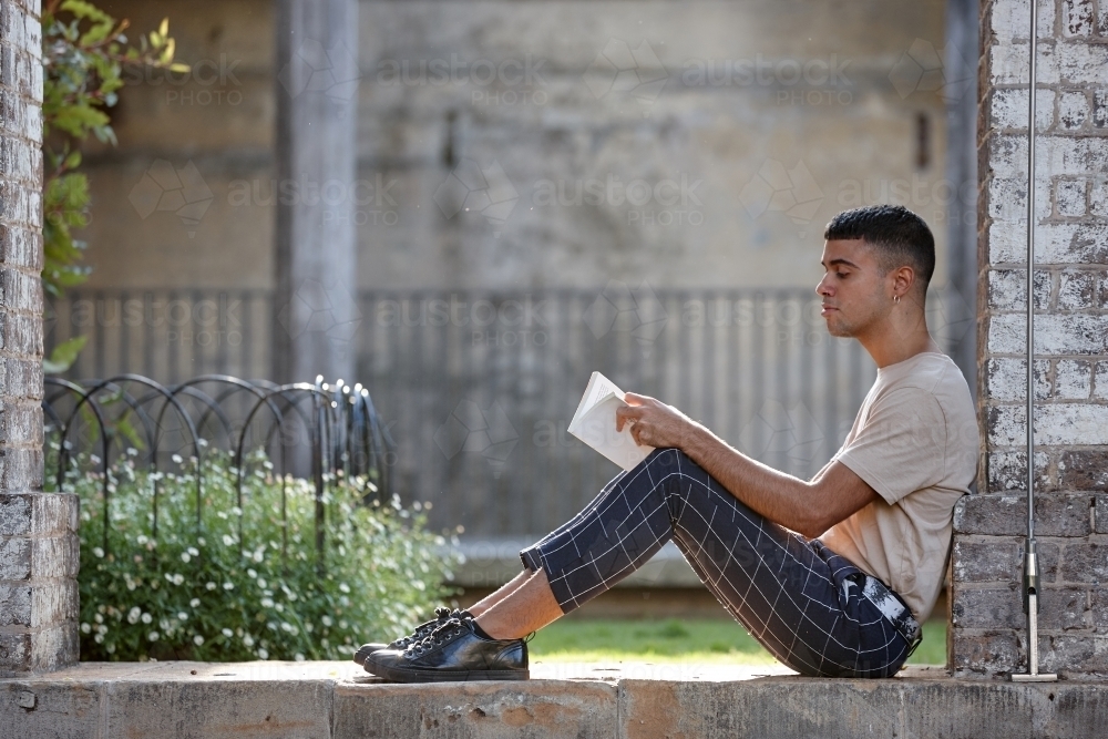 Young Indigenous Australian man enjoying time reading outdoors - Australian Stock Image