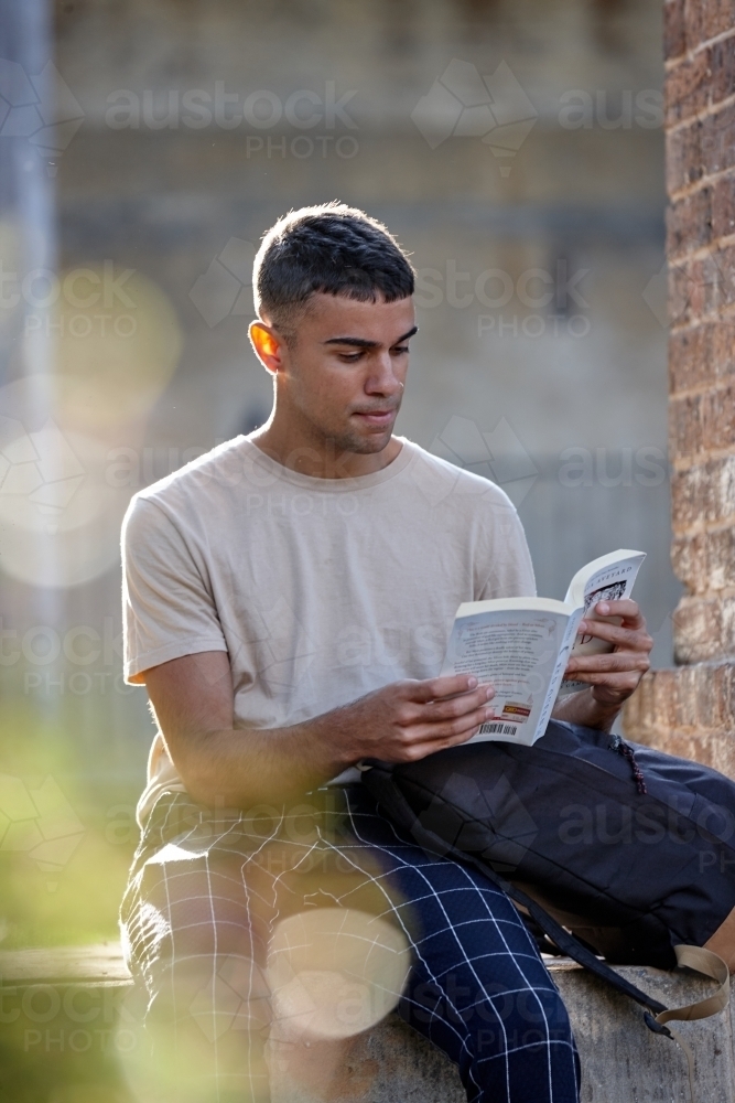 Young Indigenous Australian man enjoying time reading outdoors - Australian Stock Image