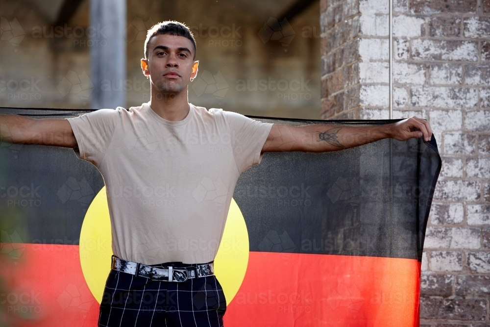 Young Indigenous Australian man holding Aboriginal flag - Australian Stock Image
