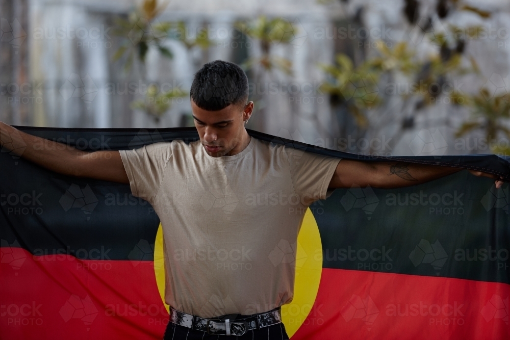 Young Indigenous Australian man holding Aboriginal flag - Australian Stock Image