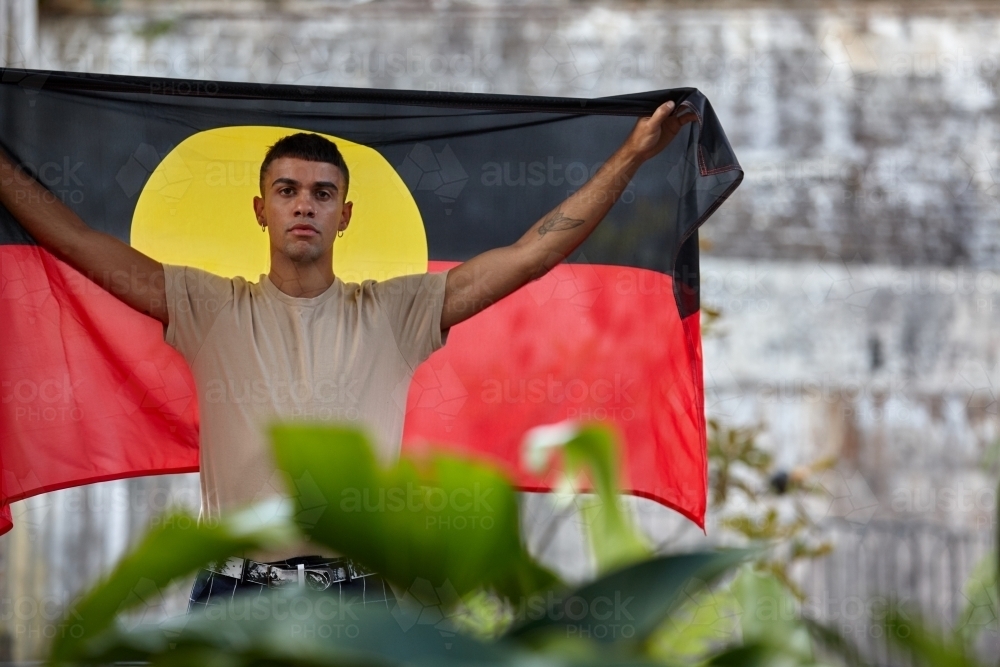 Young Indigenous Australian man holding Aboriginal flag - Australian Stock Image