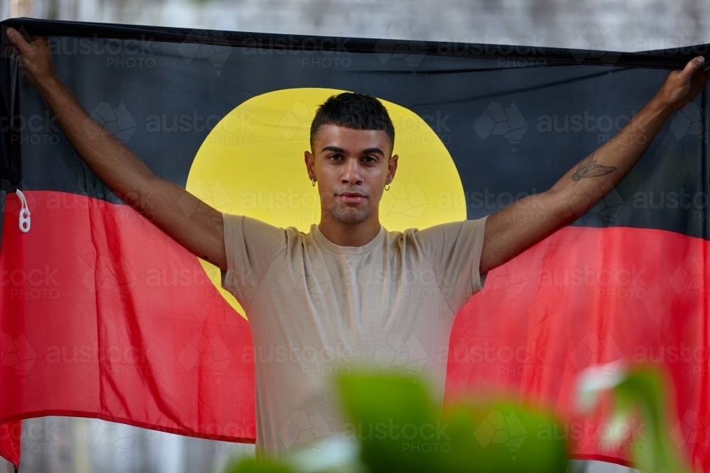 Young Indigenous Australian man holding Aboriginal flag - Australian Stock Image