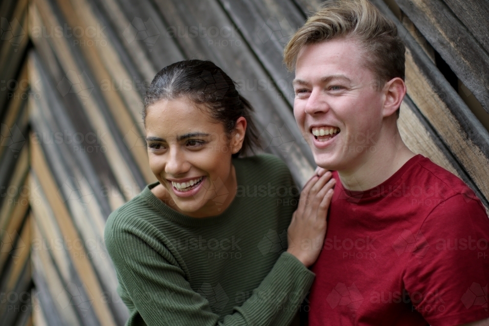 Young interracial couple laughing together in front of textured wooden panels - Australian Stock Image