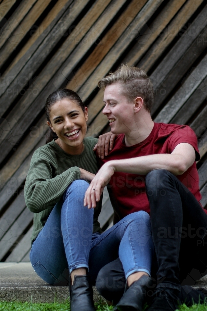 Young interracial couple laughing together in front of textured wooden panels - Australian Stock Image