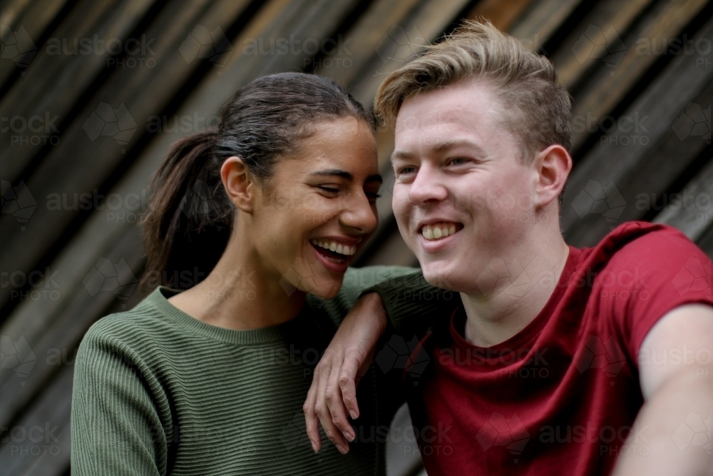 Young interracial couple laughing together in front of textured wooden panels - Australian Stock Image