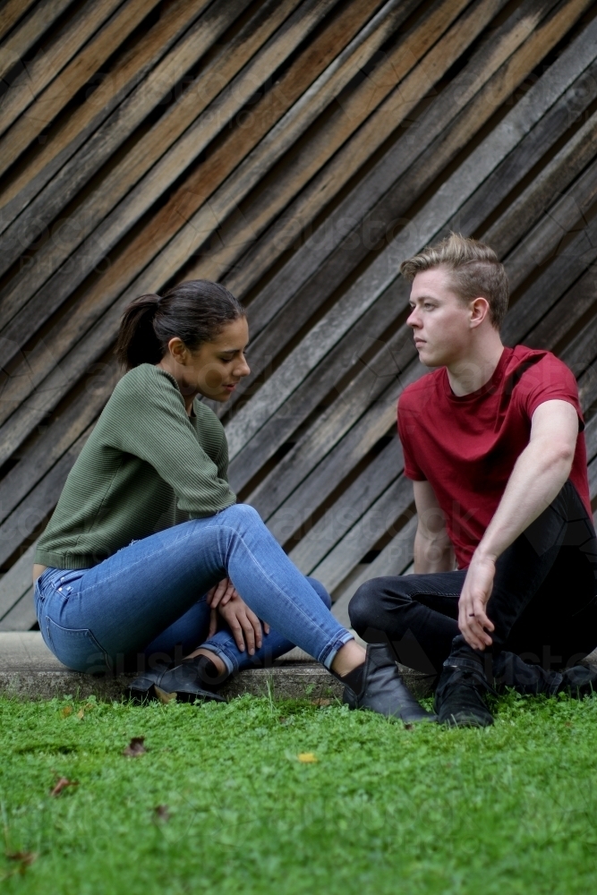Young interracial couple sitting on the ground and having a tense conversation - Australian Stock Image
