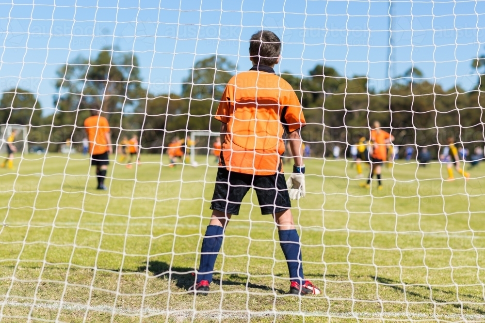 Young kid goal keeper behind net in soccer game - Australian Stock Image
