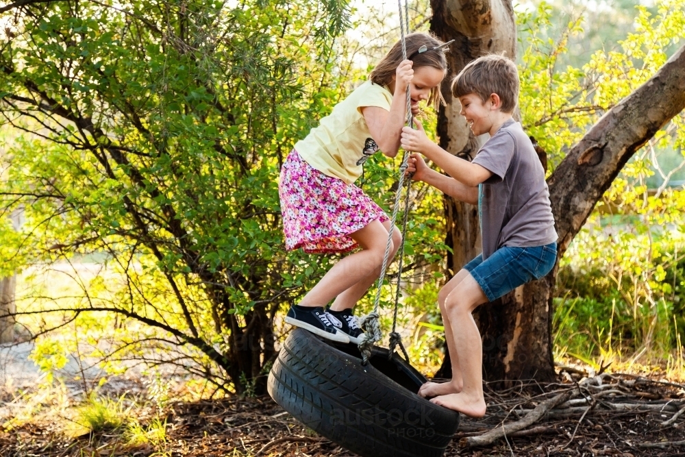 Young kids playing together on tire swing in backyard - Australian Stock Image