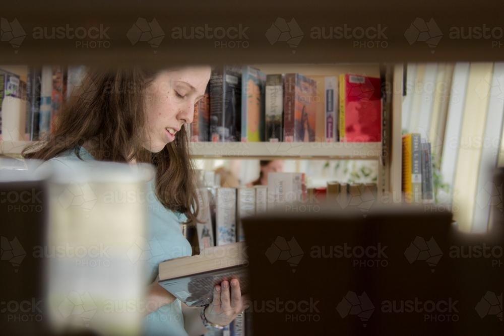 Young lady choosing a book to read from the local library - Australian Stock Image