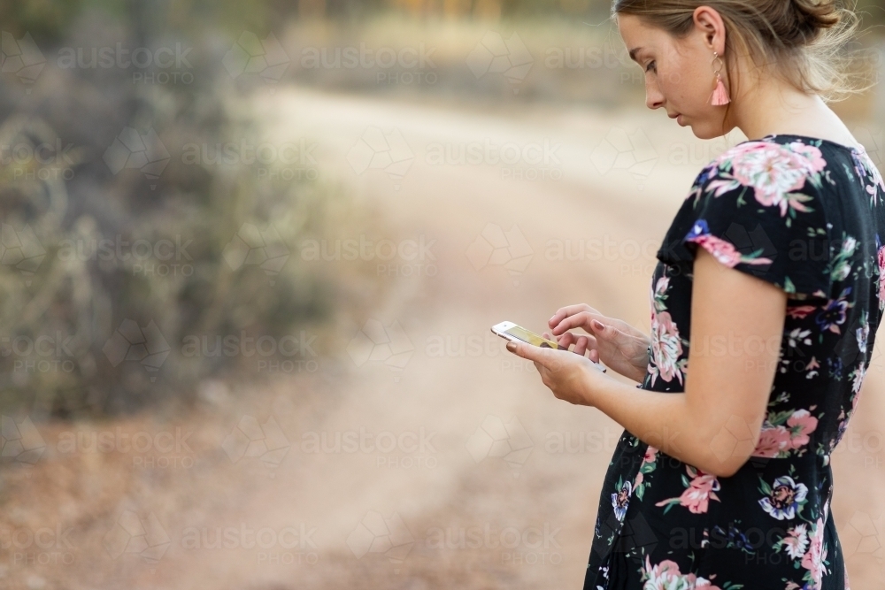 young lady in rural setting looking at her mobile phone - Australian Stock Image