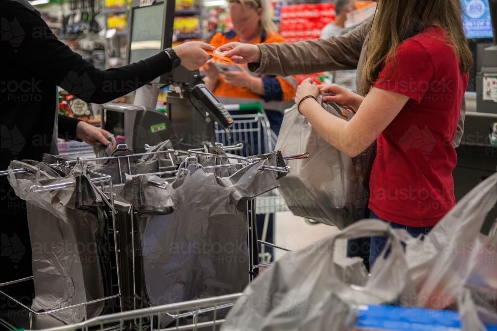Young lady paying for purchases with debit card and packing trolley with shopping - Australian Stock Image