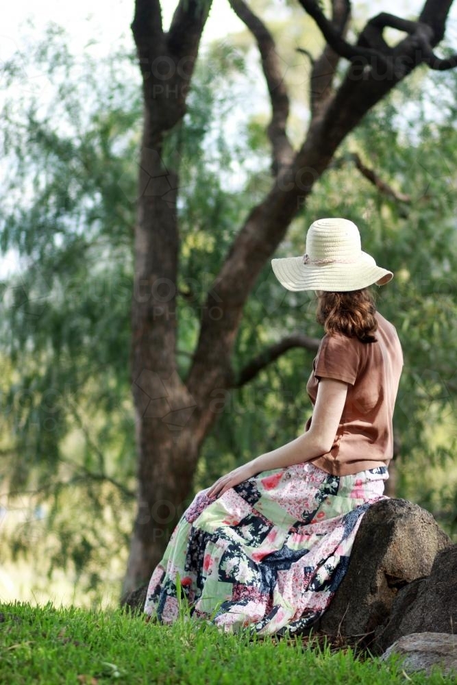 Young lady sitting on a rock in a park looking away - Australian Stock Image