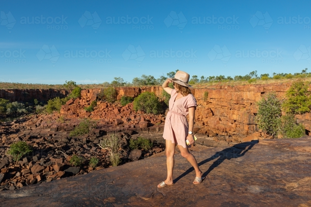 young lady tourist holding her hat while walking on rocky ledge in the Kimberley - Australian Stock Image