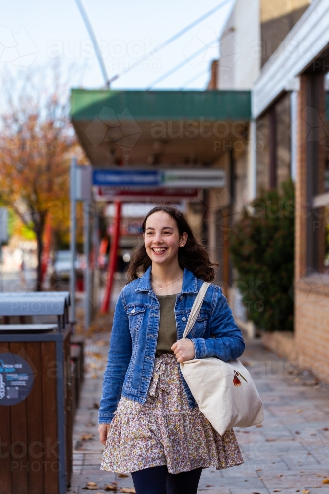 Young lady walking down street of country town in winter carrying bag - Australian Stock Image