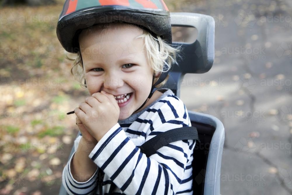 Young laughing boy wearing helmet in bike seat - Australian Stock Image
