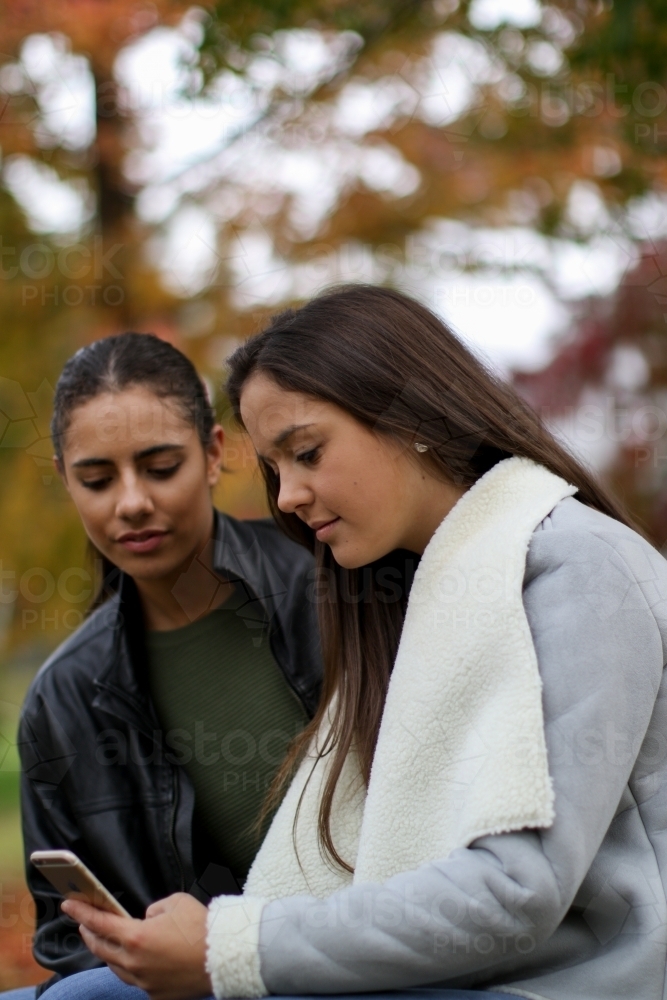 Young lesbian couple both looking down at phone - Australian Stock Image